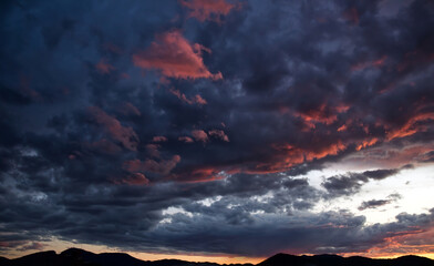 Colorful evening sky with dramatic clouds displaying beautiful orange, pink, and purple hues over a dark mountain silhouette.