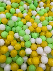 Vibrant mix of yellow, green, and white plastic balls in a children's ball pit, creating a playful and colorful texture background.