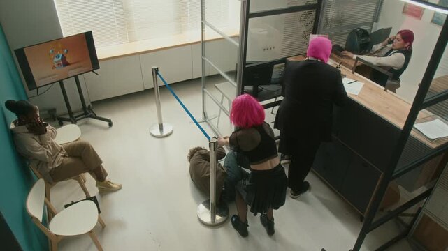 High angle shot of female and male robbers disguised by pink wig and balaclava breaking into bank threatening scared customers and teller with guns demanding money