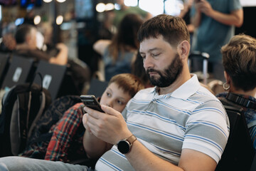 father and son browsing in smartphones, playing game, texting messages waiting for flight in airport