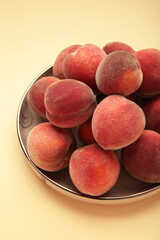 Sweet peaches and leaves on dark plate on beige background. Vertical photo