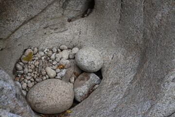 A natural stone hollow filled with smooth pebbles and larger round rocks. The textures and earthy...