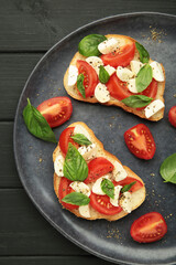 Tasty sandwich with mozzarella cheese, tomatoes and basil on cutting board on black wooden background. Caprese