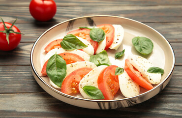 Italian Caprese salad with cherry tomatoes, mozzarella, basil on plate on brown background.