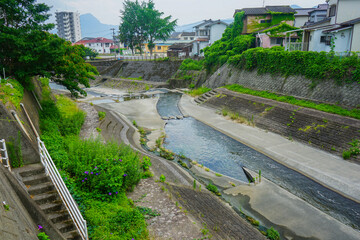 Water drainage river with staircase and foliage going through a residential area of town along a walking path near Beppu University in Beppu, Oita, Japan