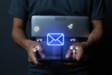 Person holding a phone with email and social media icons and a laptop behind it