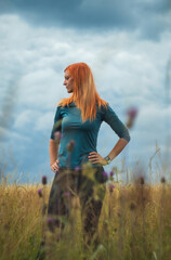Portrait of redhair woman standing in rural meadow landscape with overcast sky