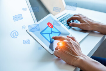 Person using laptop and tablet with email notification on white desk in bright light setting