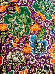Beautiful Indonesian batik fabric with floral and leaf motifs. Painted in detail. Dominated by orange, green and blue, isolated on purple background. Suitable for background and texture ideas