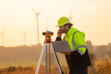 Engineer working on laptop in front of wind turbines for checking wind turbines of the field during beautiful sunset. Alternative energy concept.