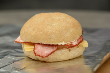 A sandwich with smoked sausage and yellow cheese on a white wheat roll, a second breakfast for school, a takeaway meal