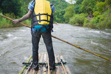 Man with yellow life jacket standing on a wooden raft on the river.