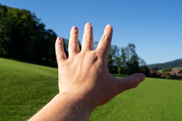 Hand reaching out over green landscape 