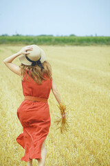 Woman in red linen dress running through wheat field holding straw bouquet, enjoying rural freedom...