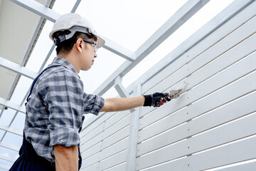 Asian male construction worker using plastering trowel for bolt head grouting on white wooden wall panel. Construction defect repair process