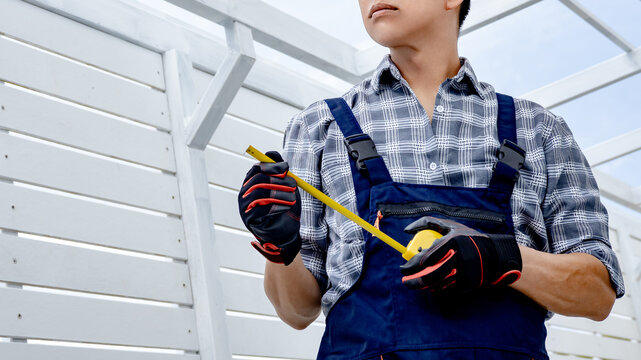 Half face of Asian man civil engineer holding tape measure at construction site. Confident male construction worker in protective workwear looking forward