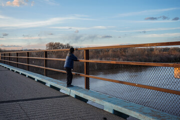 Man stands on bridge overlooking the Rio Grande River in Albuquerque, New Mexico, USA at sunset