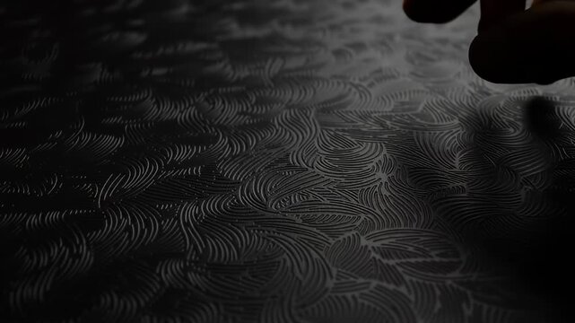 Intricate wave-like pattern embossed on a surface, subtly illuminated in a dark tone