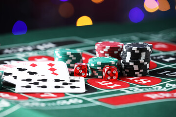Casino chips, dice and playing cards on roulette table against blurred lights, closeup