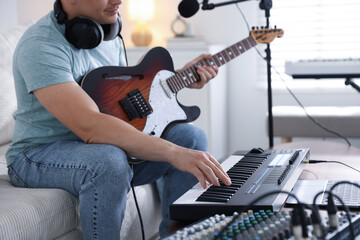 Man working with MIDI keyboard and guitar on sofa in home studio, closeup
