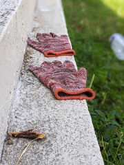 A pair of knitted work gloves resting on a textured concrete ledge outdoors, with blurry background...
