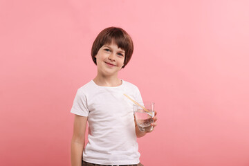 Cute little boy with glass of refreshing soda drink on pink background