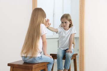 Upset little girl looking at herself in mirror indoors