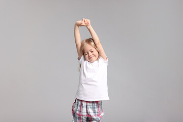 Cute little girl in pajamas stretching on grey background