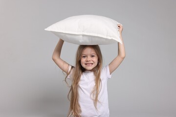 Cute little girl in pajamas with pillow on grey background