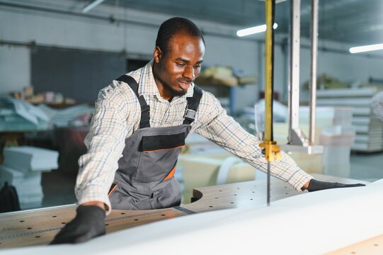 African american Furniture maker cutting fabric with electric saw in factory