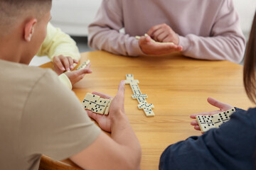 Friends playing dominoes at wooden table indoors, closeup