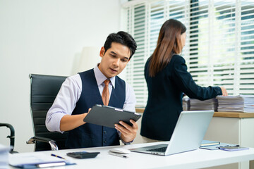 Confident business team in office attire reviewing documents and tablet, showcasing teamwork,...
