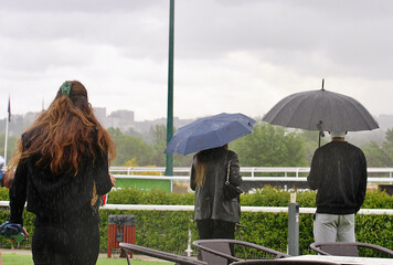 Tormenta con lluvia, nubes y personas con paraguas bajo la lluvia en el hipódromo de Madrid