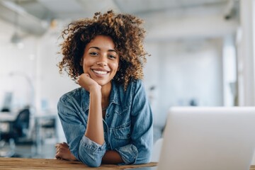 Smiling young woman working on laptop in modern office environment with natural light.