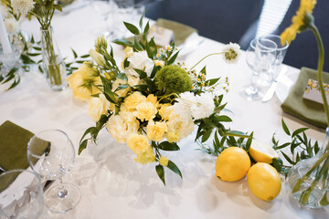 Festive table in yellow and white decor with flowers and lemons.