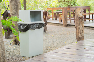 Grey trash bin positioned near a wooden wall in a public area. Grey garbage bin outdoors in summer.