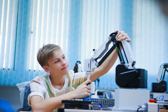 Young male student interacting with robot arm in school lab, exploring engineering concepts and building problem-solving skills. - Powered by Adobe