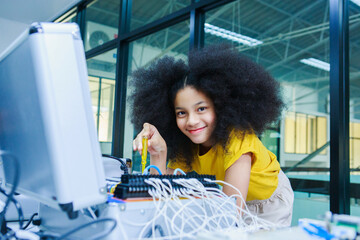Young Black girl in yellow shirt assembling electronics with wires and microcontroller in...