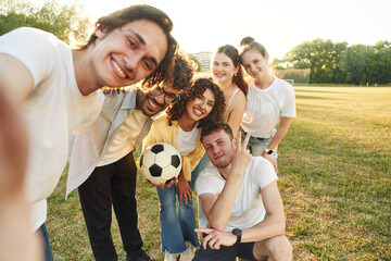 Obraz premium Handsome man is doing a selfie. Young friends are having fun on the field with soccer ball
