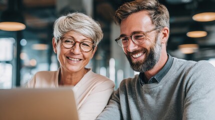 Happy senior woman and young man working together on a laptop in a modern office environment.