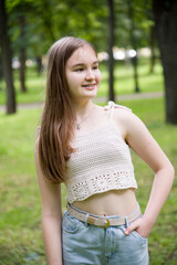 young brunette smiling woman in hand made top posing in sunny park near tree on summer 