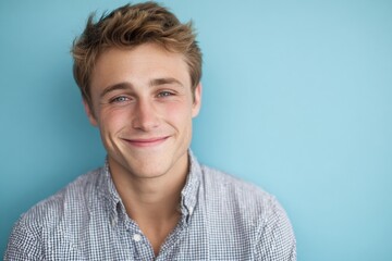 Fototapeta premium Happy young man with light brown hair and casual shirt smiling against blue background.