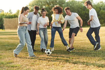 In the casual clothes. Group of friends are playing soccer on the field