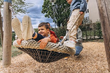 Happy family with two sons playing together on a large rope swing at playground. Parents smiling,...