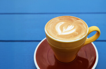 Frothy cappuccino coffee in yellow brown cup isolated on blue wooden table