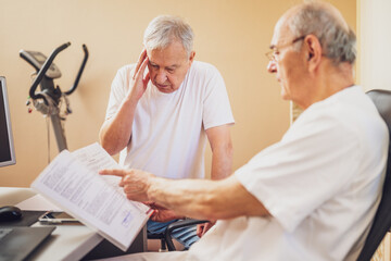 Patient is having exam at cardiologist. Doctor is looking at his medical files. Patient is...