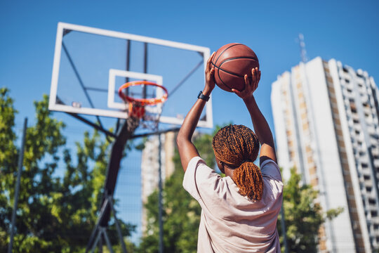 Young woman practicing basketball alone at sports court in the morning. She is taking a shot on basket. - Powered by Adobe
