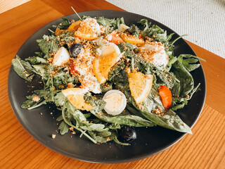 A vibrant salad featuring fresh greens, colorful fruits, and crunchy toppings arranged on a sleek black plate.