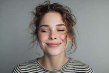 Fototapeta premium Smiling young woman with curly hair and relaxed expression against plain wall.