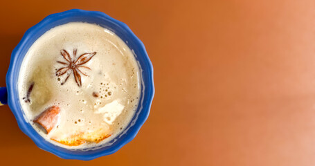 A beautifully frothy cup of spiced beverage with star anise on top, set against a warm brown background.